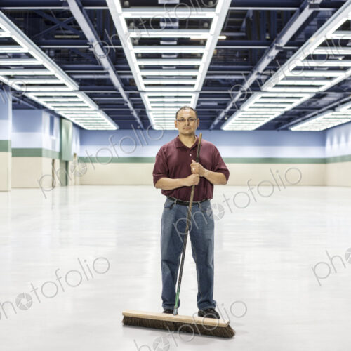 An hispanic man standing with a broom in a large convention cener space.