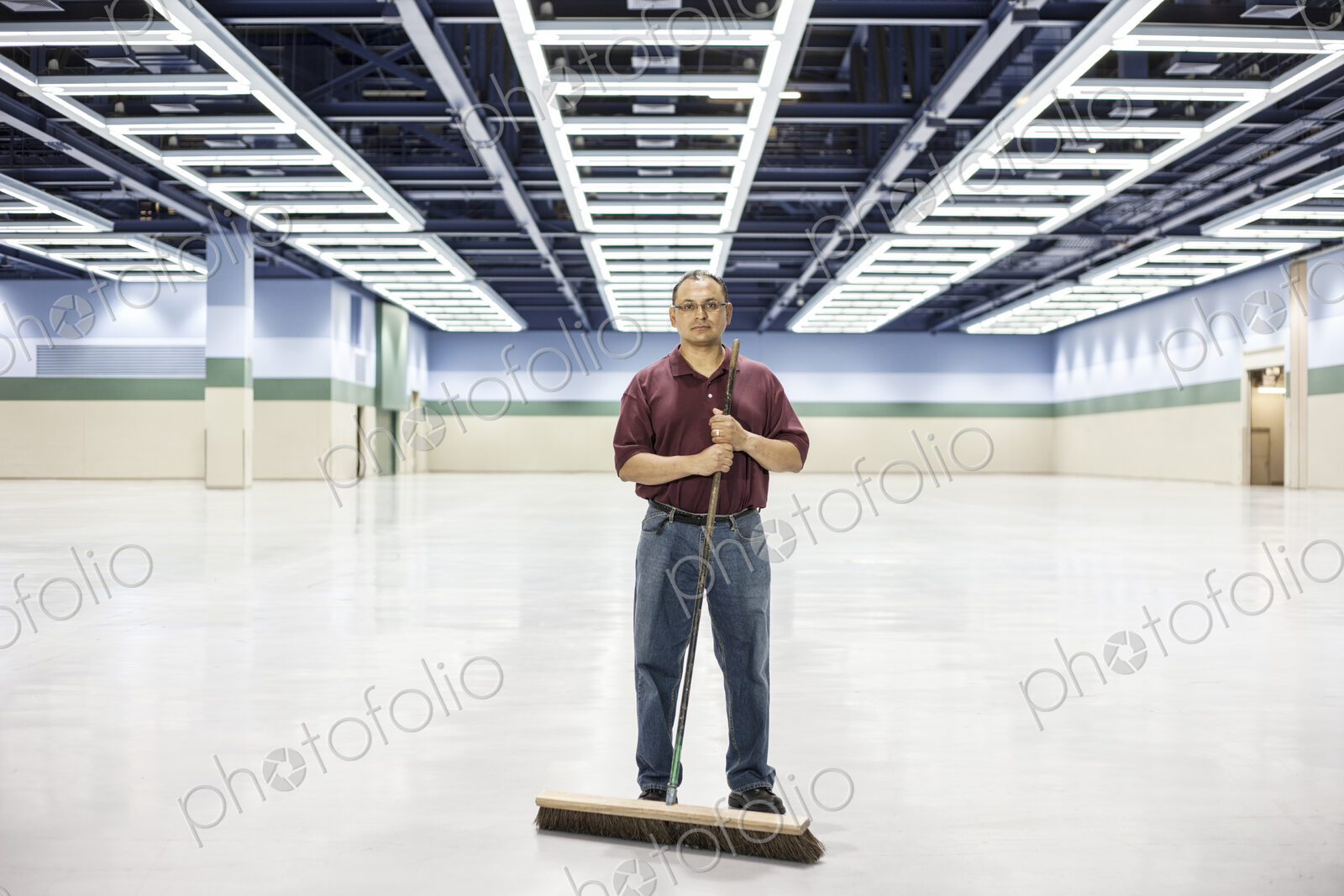 An hispanic man standing with a broom in a large convention cener space.