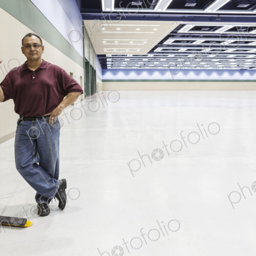 An hispanic workman standing in a large interior space with a broom.