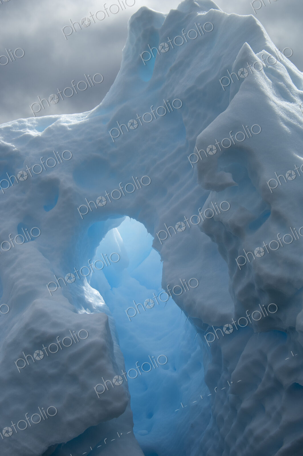 An iceberg with a natural arch and translucent glow, with sunlight shining through the…