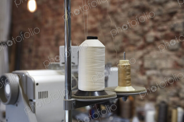 An industtrial sewing machine in a leather workshop, with a bare brick wall in the…