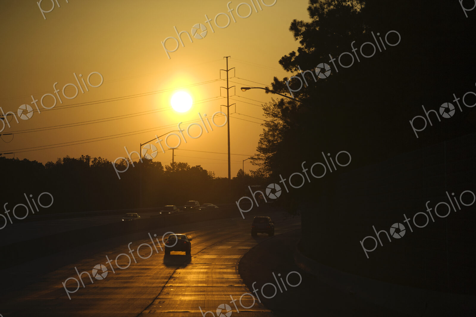 An interstate highway, road bordered by trees, a car driving into the sunset.