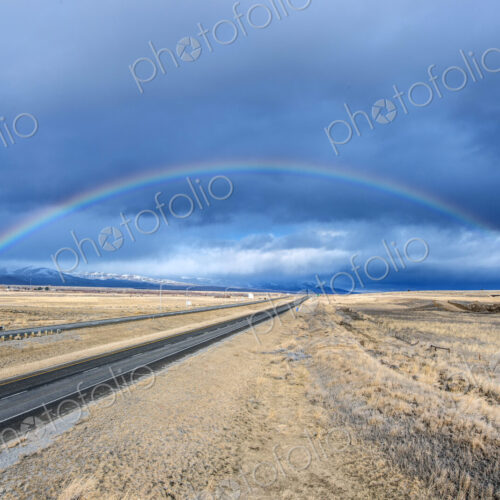 An interstate road reaching to the horizon through a flat landscape, rainbow above the… An interstate road reaching to the horizon through a flat landscape, rainbow above the…