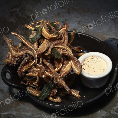 An iron skillet with tempura, fried food in batter, and a small dish of sauce.