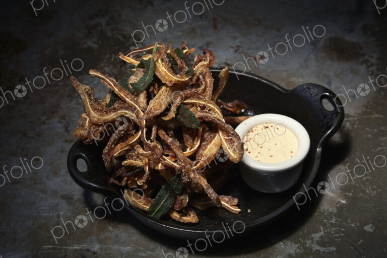 An iron skillet with tempura, fried food in batter, and a small dish of sauce.