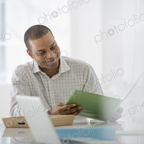 An office in the city. Business. A man seated at a desk opening a file of paperwork. A…