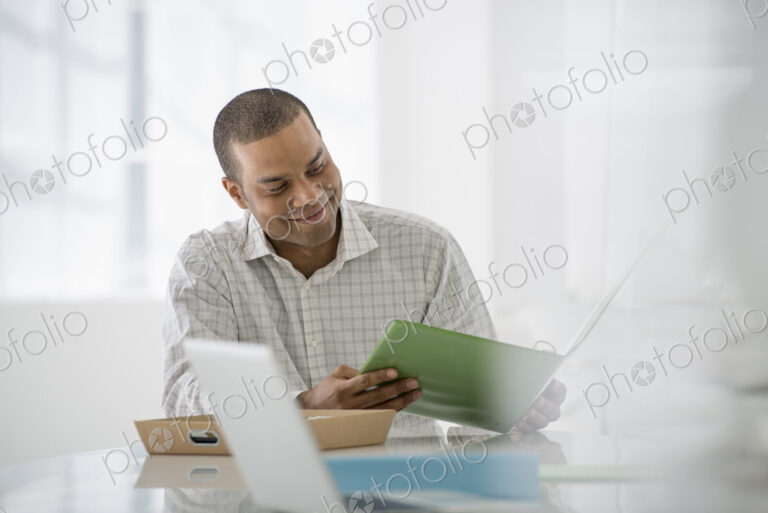 An office in the city. Business. A man seated at a desk opening a file of paperwork. A…