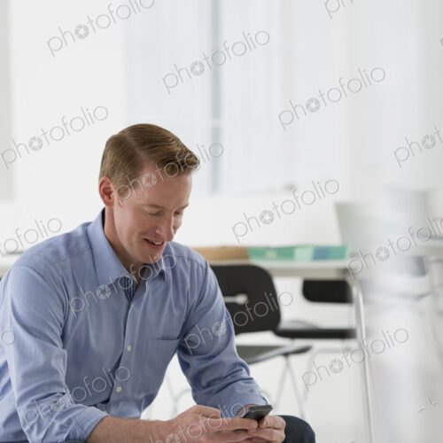 An office in the city. Business. A man seated, checking his smart phone for messages…