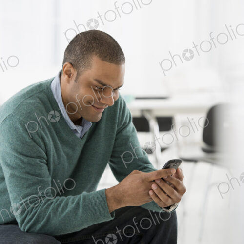 An office in the city. Business. A man seated, checking his smart phone for messages… An office in the city. Business. A man seated, checking his smart phone for messages…