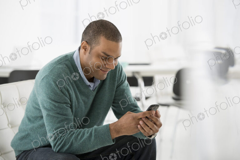 An office in the city. Business. A man seated, checking his smart phone for messages…