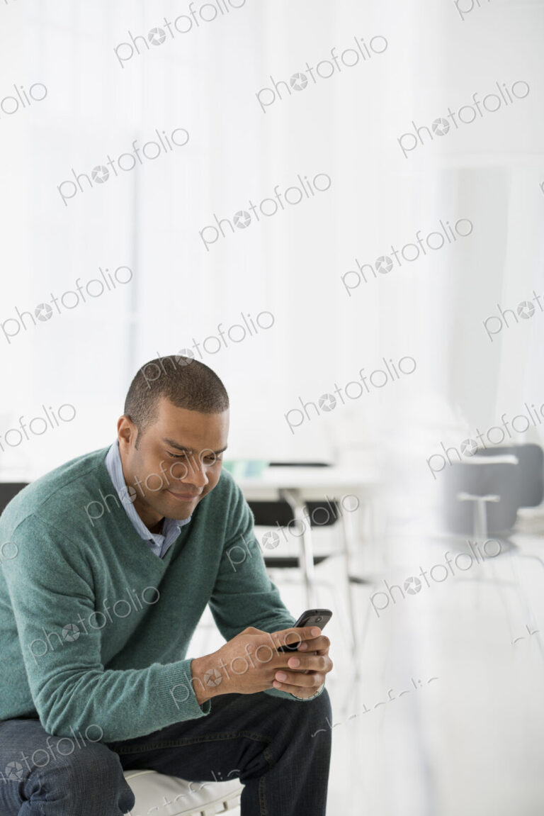 An office in the city. Business. A man seated, checking his smart phone for messages…