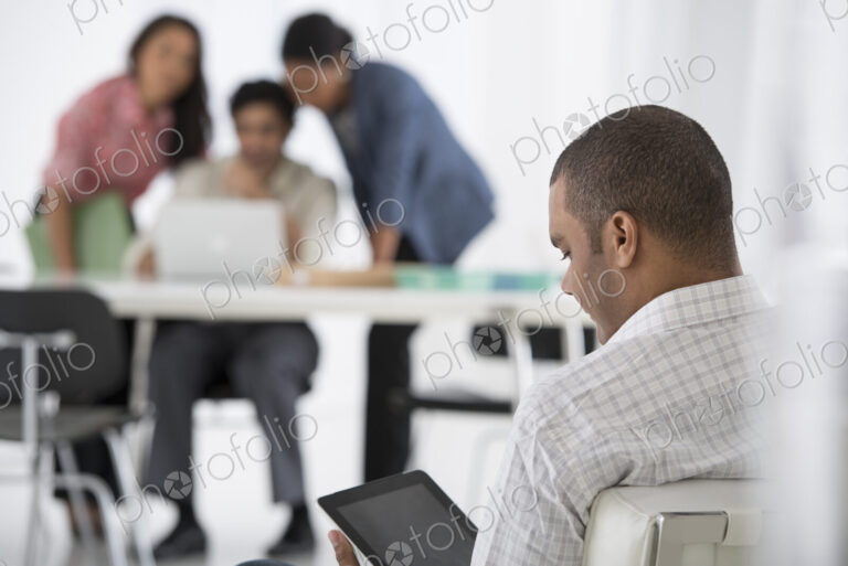 An office in the city. Business. A man seated in the foreground, and three people…