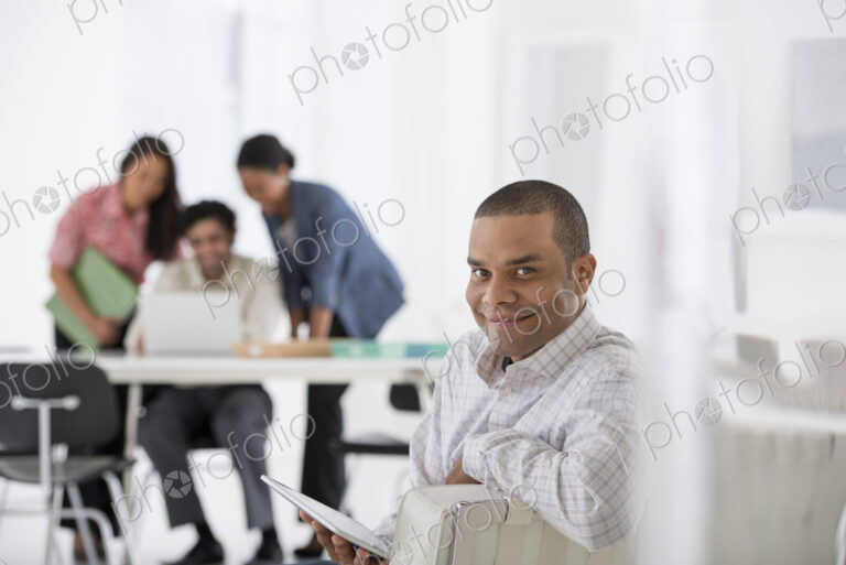 An office in the city. Business. A man seated in the foreground, and three people…