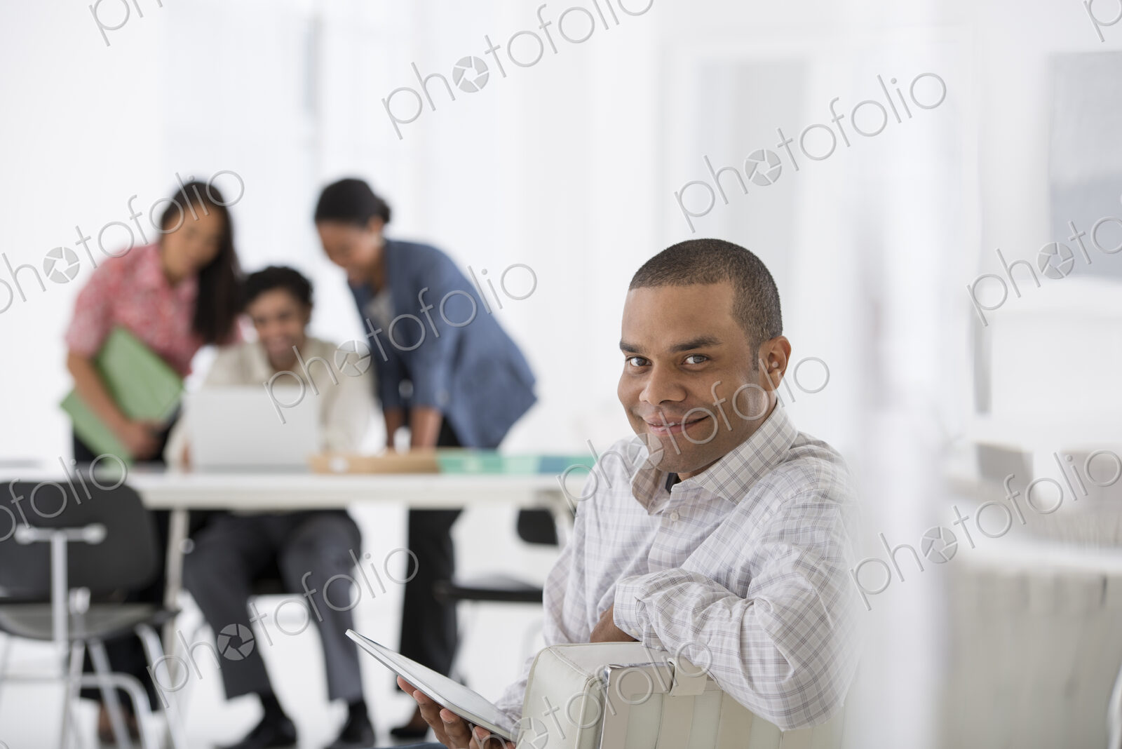 An office in the city. Business. A man seated in the foreground, and three people…