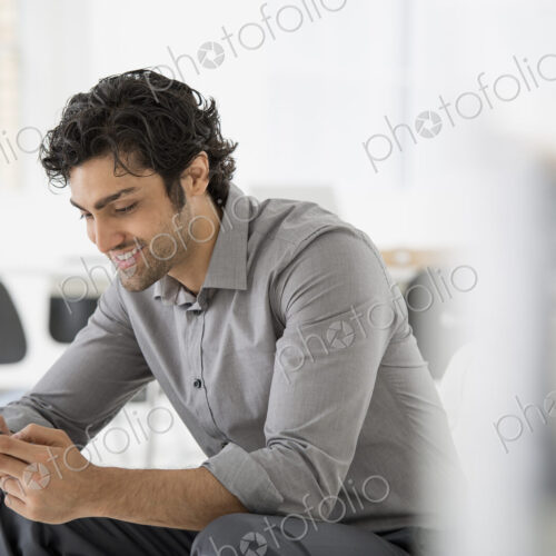 An office in the city. Business. A man seated looking at the screen on his smart phone. An office in the city. Business. A man seated looking at the screen on his smart phone.