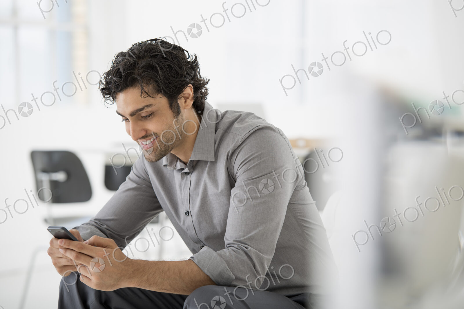 An office in the city. Business. A man seated looking at the screen on his smart phone.