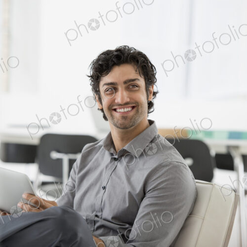 An office in the city. Business. A man seated smiling and holding a digital tablet. An office in the city. Business. A man seated smiling and holding a digital tablet.