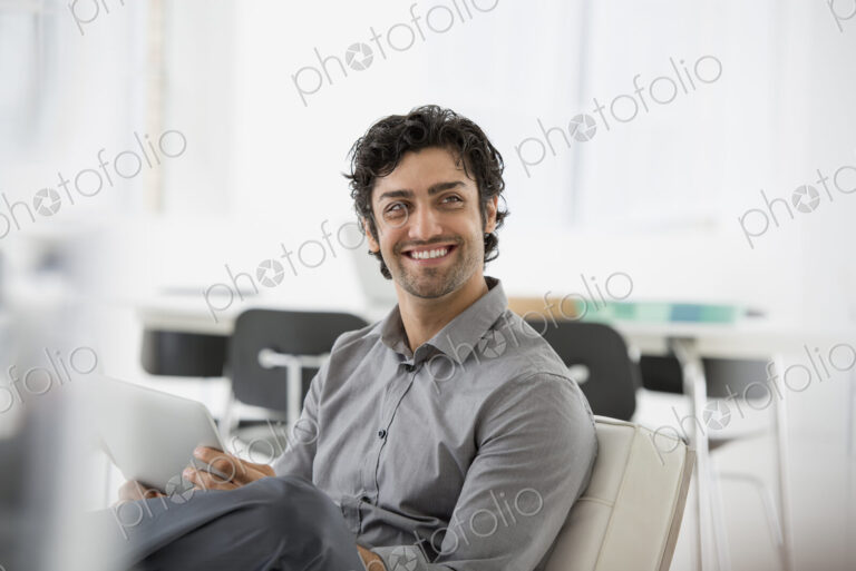 An office in the city. Business. A man seated smiling and holding a digital tablet.