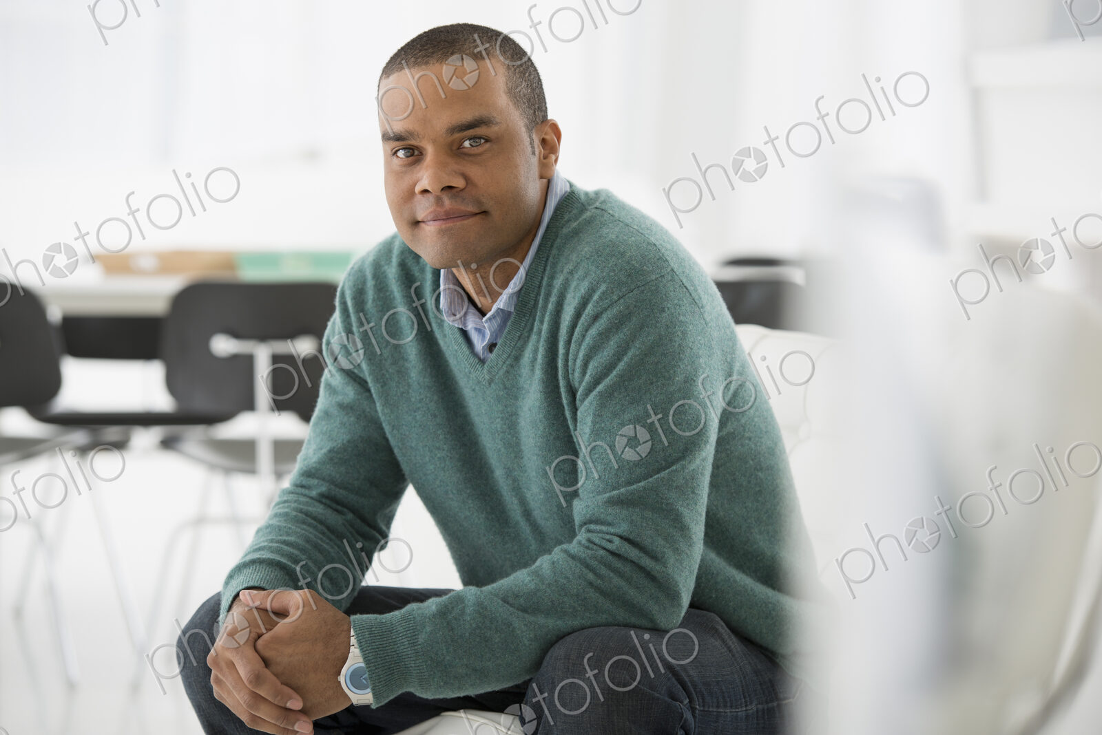 An office in the city. Business. A man sitting, hands clasped in a relaxed confident pose.