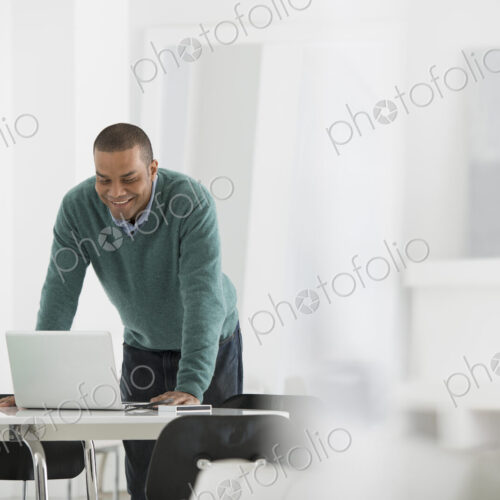 An office in the city. Business. A man standing over a desk, leaning down to use a… An office in the city. Business. A man standing over a desk, leaning down to use a…