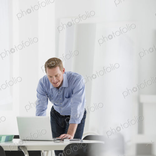 An office in the city. Business. A man standing over a desk, leaning down to use a… An office in the city. Business. A man standing over a desk, leaning down to use a…