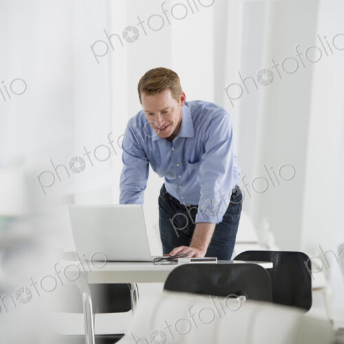 An office in the city. Business. A man standing over a desk, leaning down to use a… An office in the city. Business. A man standing over a desk, leaning down to use a…