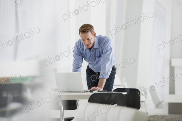 An office in the city. Business. A man standing over a desk, leaning down to use a…