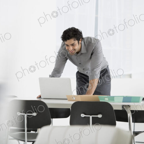 An office in the city. Business. A man standing over a desk, leaning down to use a… An office in the city. Business. A man standing over a desk, leaning down to use a…