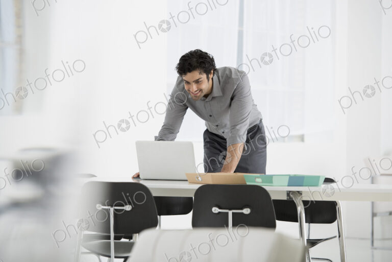 An office in the city. Business. A man standing over a desk, leaning down to use a…