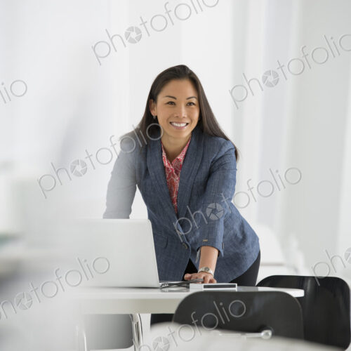 An office in the city. Business. A woman leaning over a desk using a laptop computer. An office in the city. Business. A woman leaning over a desk using a laptop computer.