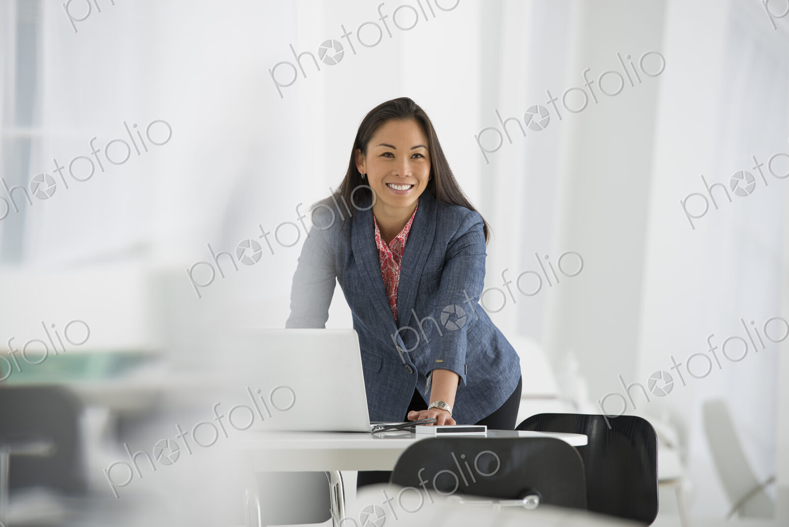 An office in the city. Business. A woman leaning over a desk using a laptop computer.
