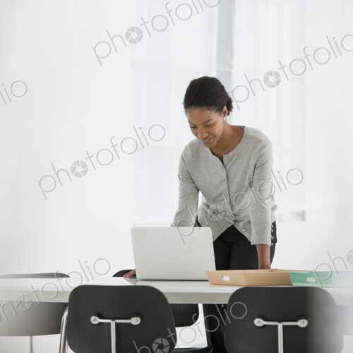 An office in the city. Business. A woman leaning over a desk using a laptop computer. An office in the city. Business. A woman leaning over a desk using a laptop computer.