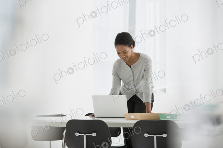 An office in the city. Business. A woman leaning over a desk using a laptop computer.
