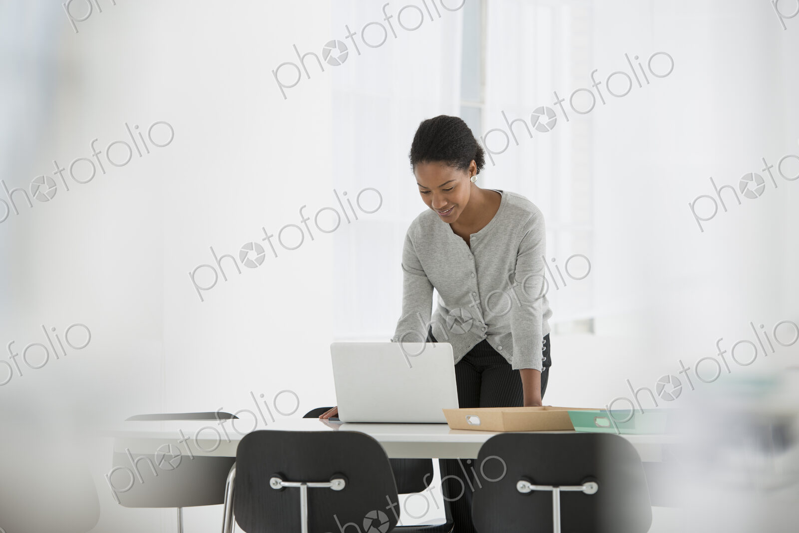 An office in the city. Business. A woman leaning over a desk using a laptop computer.