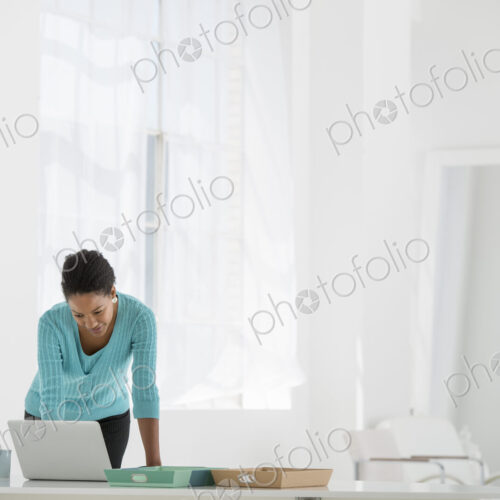 An office in the city. Business. A woman leaning over a desk using a laptop computer. An office in the city. Business. A woman leaning over a desk using a laptop computer.