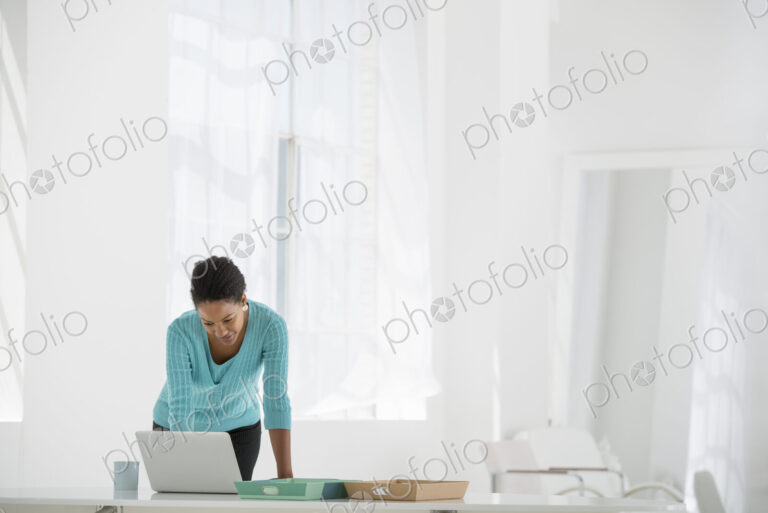 An office in the city. Business. A woman leaning over a desk using a laptop computer.