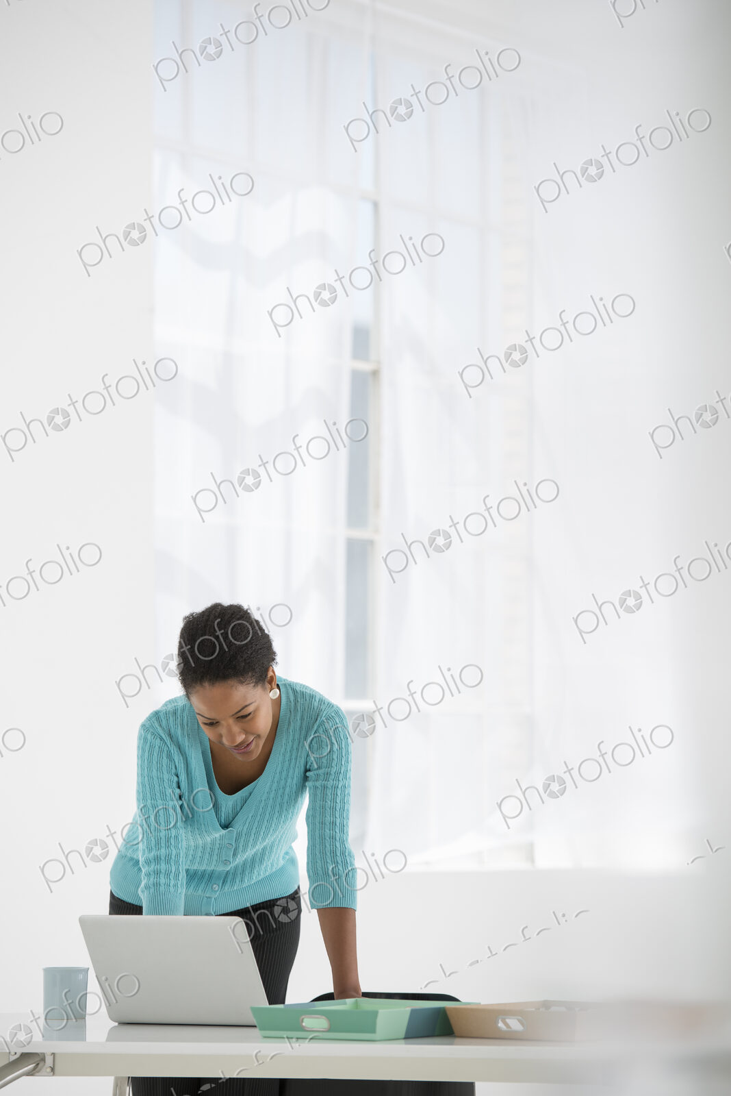 An office in the city. Business. A woman leaning over a desk using a laptop computer.