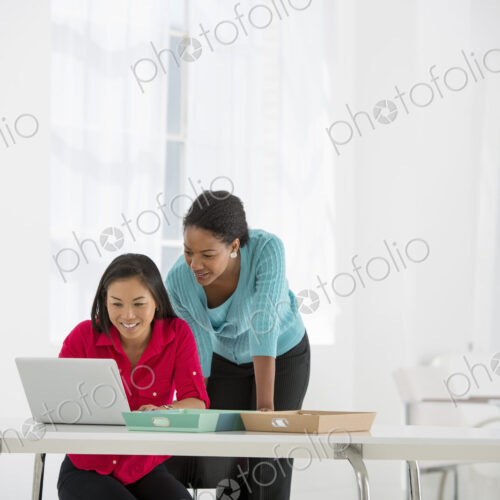 An office in the city. Business. Two women leaning over and using a laptop computer.