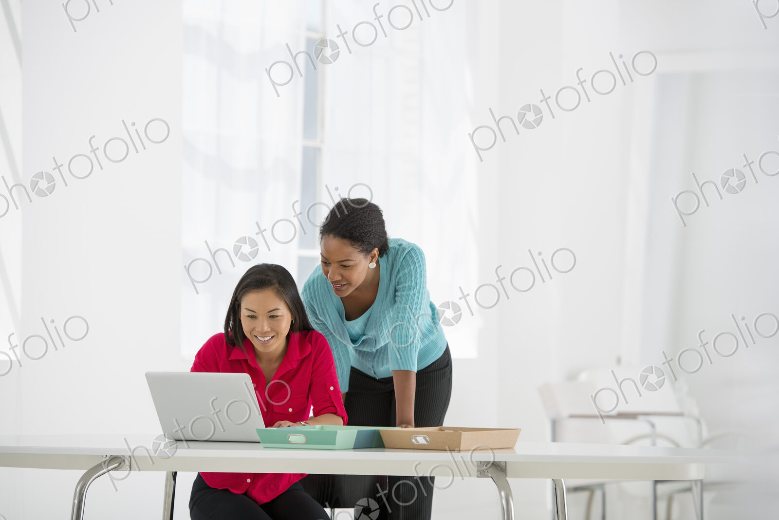An office in the city. Business. Two women leaning over and using a laptop computer.
