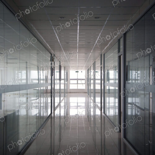 An office interior, straight wide corridor with reflective surfaces on walls and floor…