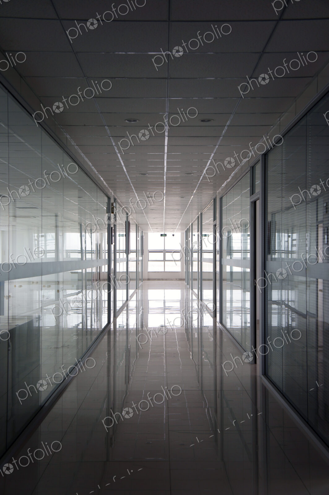 An office interior, straight wide corridor with reflective surfaces on walls and floor…