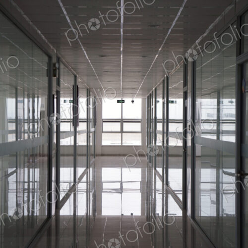 An office interior, straight wide corridor with reflective surfaces on walls and floor…