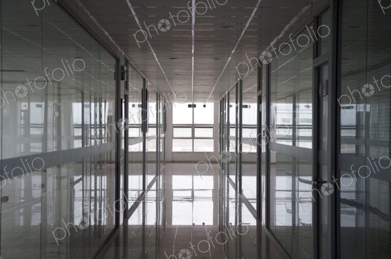 An office interior, straight wide corridor with reflective surfaces on walls and floor…