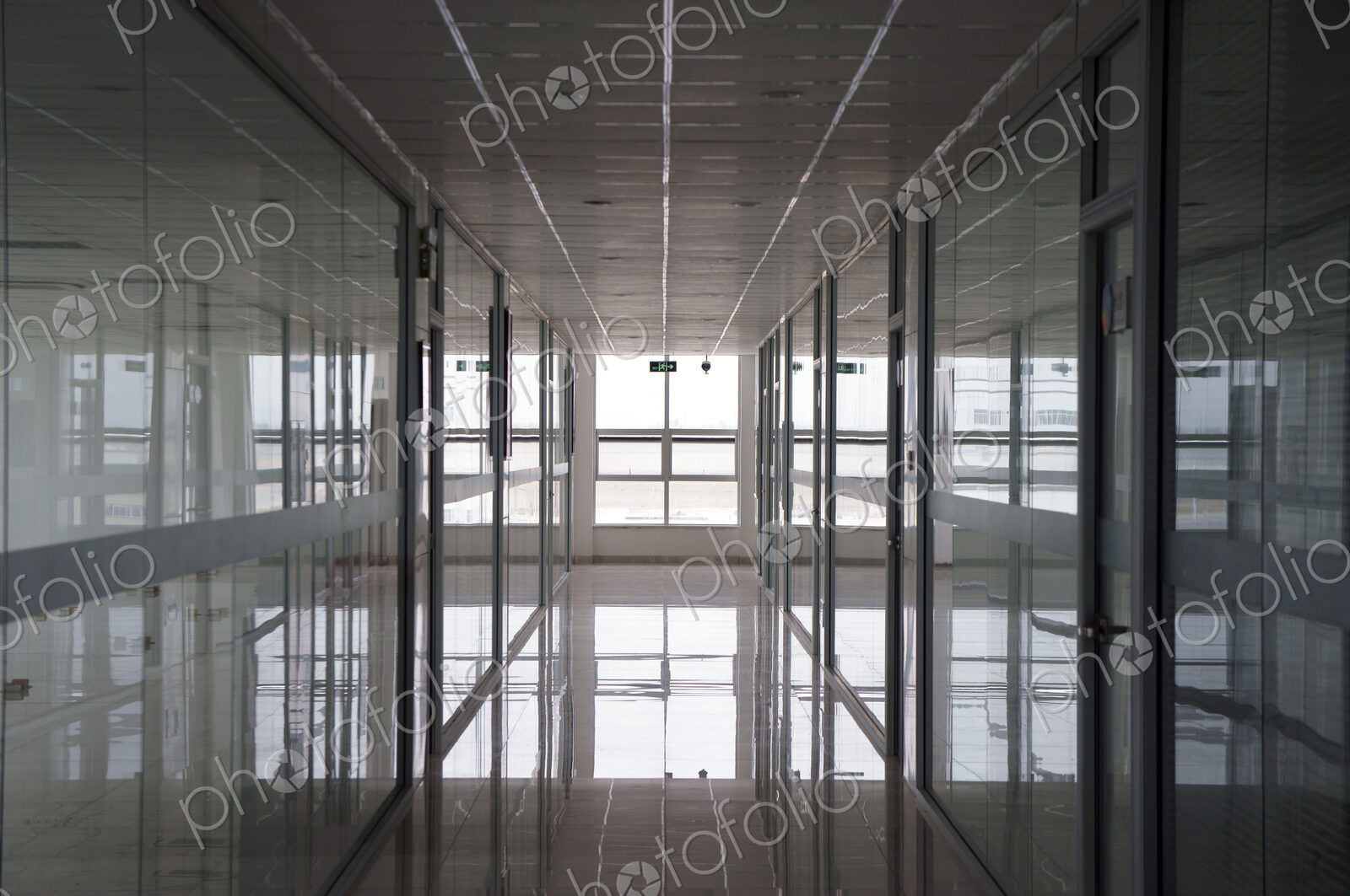 An office interior, straight wide corridor with reflective surfaces on walls and floor…