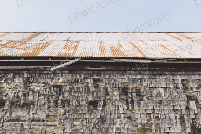 An old farmhouse with wooden shingle tiles on the walls and corrugated iron roof