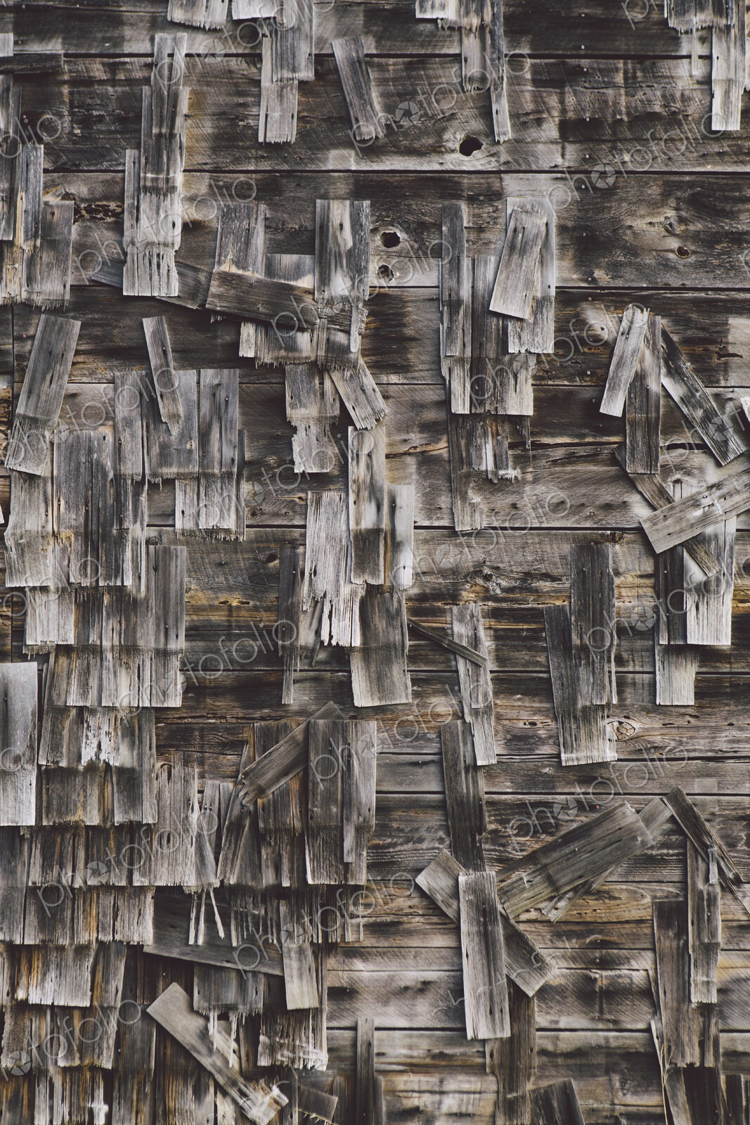 An old farmhouse with wooden shingle tiles on the walls. Silvery grey colours.