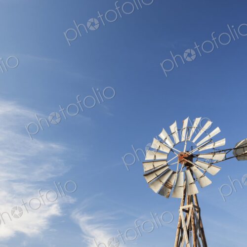 An old prairie windmill rises against a wide blue sky in South Dakota, thin clouds…