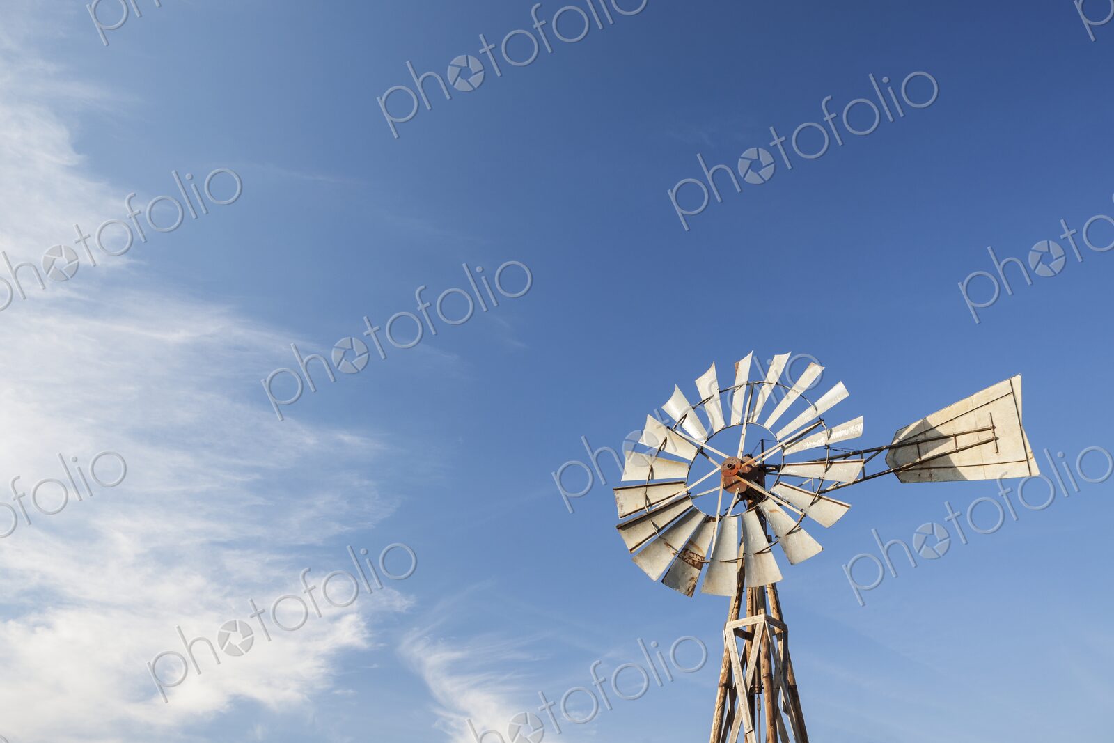 An old prairie windmill rises against a wide blue sky in South Dakota, thin clouds…
