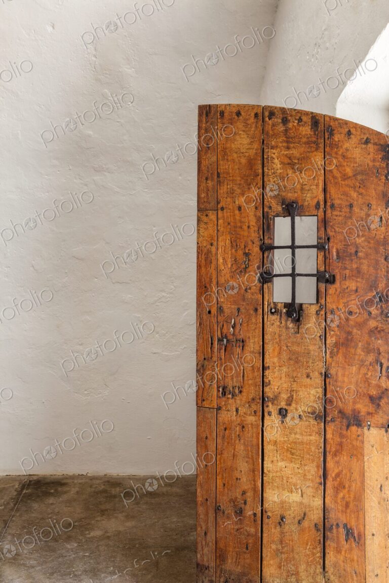 An old wooden door with iron grate detail stands partially open inside Castillo San…