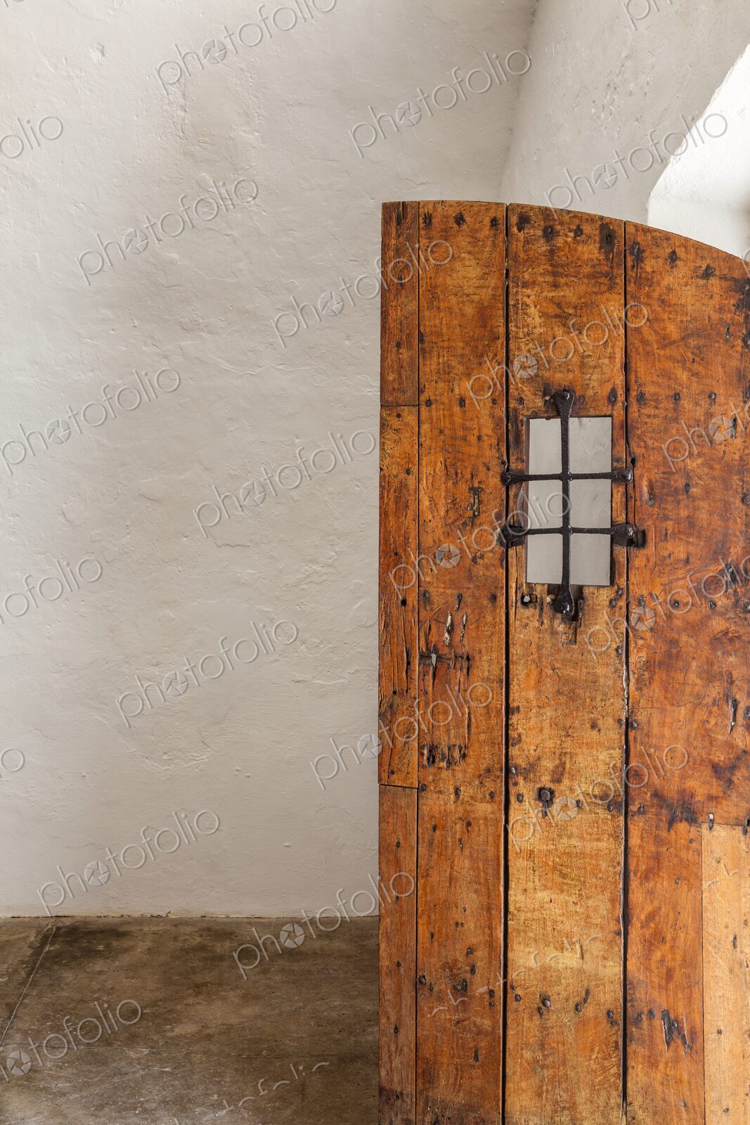 An old wooden door with iron grate detail stands partially open inside Castillo San…